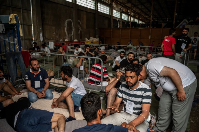Survivors of a shipwreck sit inside a warehouse at the port in Kalamata town, on June 15, 2023, after a boat carrying migrants sank in international waters in the Ionian Sea. - Greece has declared three days of mourning, the interim prime minister's office said on June 14, 2023, over a migrant boat sinking in the Ionian Sea feared to have claimed hundreds of lives. The Greek coastguard has so far recovered 79 bodies and rescued over 100, but survivors are claiming that up to 750 people were on board. (Photo by Angelos TZORTZINIS / POOL / AFP)