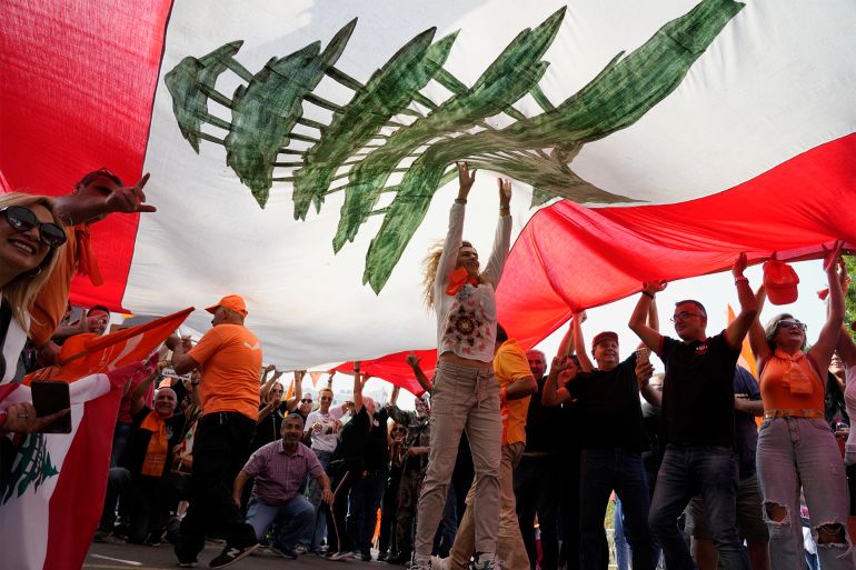 Supporters of Lebanese President Michel Aoun hold up a giant Lebanese flag as he delivers a speech outside the presidential palace in Baabda, east of Beirut, Lebanon, Sunday, Oct. 30, 2022. Aoun left Lebanon's presidential palace Sunday marking the end of his six-year term without a replacement, leaving the small nation in a political vacuum that is likely to worsen its historic economic meltdown. (AP Photo/Bilal Hussein) AP22303479350676