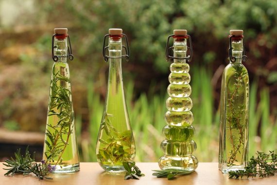 herb infused oils in decorative glass bottles with herb leaves backlit with a garden background GettyImages-145907494