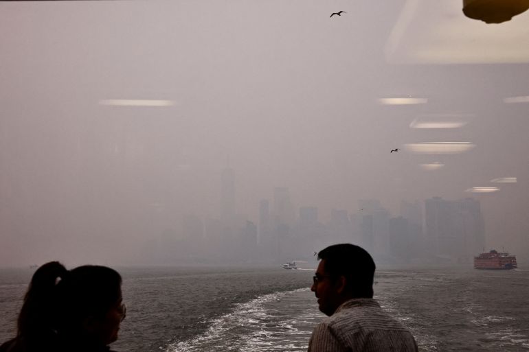 Commuters stand on the Staten Island Ferry while the Manhattan skyline is seen in the background covered by haze and smoke caused by wildfires in Canada, in New York