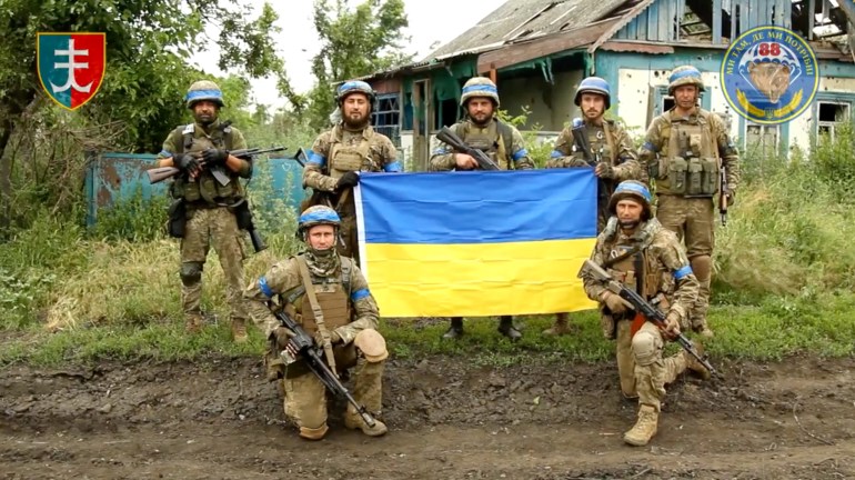 Ukrainian servicemen pose for a photograph with the Ukrainian flag in the liberated village of Storozheve, in Dontesk region