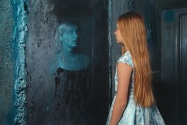 Lunatic young girl looking in the mirror and seeing in reflection a ghost of murdered woman shutterstock_1199782672