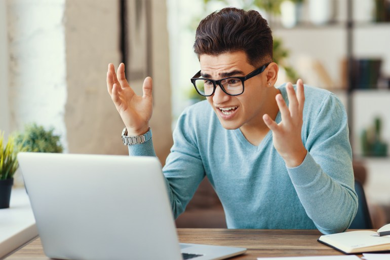 Young ethnic guy in glasses gesticulating in frustration after discovering mistake in remote project on laptop while working at home shutterstock_1788596957