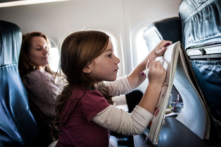 Girl (6yrs) on airplane, drawing on tablet - stock photo