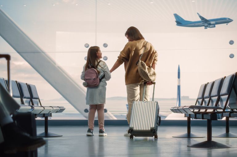 Airport Terminal: Beautiful Mother and Cute Little Daughter Wait for their Vacation Flight, Looking out of Window for Arriving and Departing Airplanes. Young Family in Boarding Lounge of Airline Hub; Shutterstock ID 2137645195; purchase_order: aljazeera ; job: ; client: ; other:
