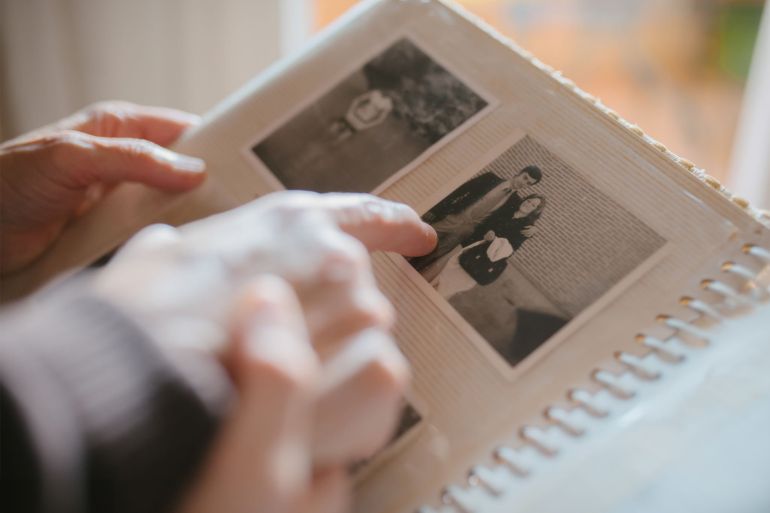 Grandmother sharing memories and stories with her granddaughter while showing her an old family photo album. - stock photo Close up view of a grandmother sharing memories and stories with her granddaughter while showing her an old family photo album. Memories and family concept.