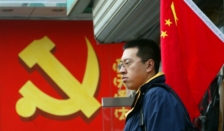 A man stands between a Chinese national flag (R) and the hammer and sickle logo of the Chinese Communist Party in Beijing November 6, 2002. The 16th Party Congress is due to open on November 8 in China's capital with a major leadership reshuffle expected. REUTERS/Guang Niu GN/RCS