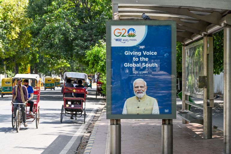 People travel on cycle rickshaws near a bus shelter displaying a G20 communication with a portrait of India's Prime Minister Narendra Modi, in New Delhi on September 4, 2023. (Photo by Sajjad HUSSAIN / AFP)