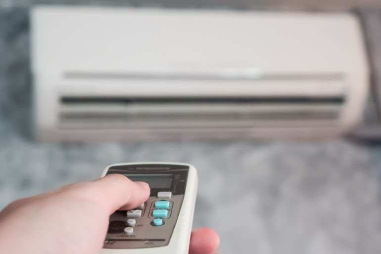 Hand holding remote in front of air conditioner.; Shutterstock ID 649767889; purchase_order: aljazeera ; job: ; client: ; other: