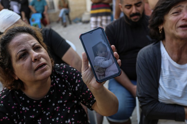 A woman shows a picture of a baby, George Ramez al-Souri, one of the 18 dead following an Israeli air strike on the Orthodox church in Gaza City [Abdelhakim Abu Riash/Al Jazeera]