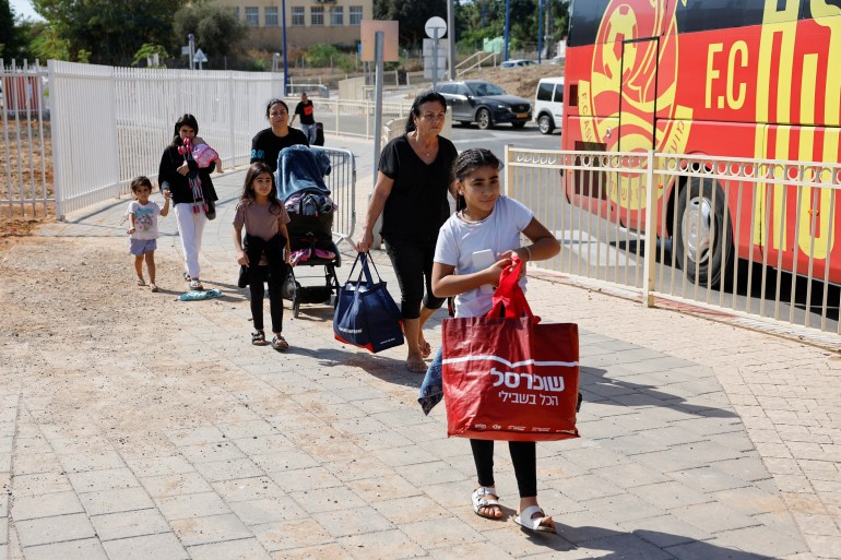 People walk with their belongings next to a bus as Israelis are evacuated from the southern town of Sderot, near Israel's border with Gaza, October 15, 2023. REUTERS/Amir Cohen