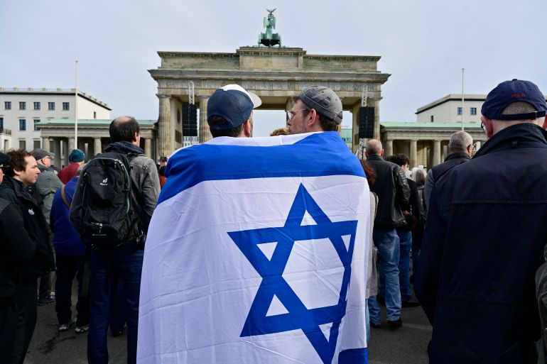 Two demonstrators are wrapped into an Israeli flag as they attend a rally in solidarity with Israel in front of the Brandenburg Gate in Berlin, Germany on October 22, 2023. (Photo by John MACDOUGALL / AFP)