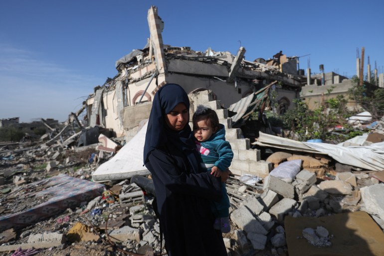 A Palestinian woman carries a child as she walks next to houses destroyed in an Israeli strike during the conflict, amid the temporary truce between Hamas and Israel, in Khan Younis in the southern Gaza Strip November 24, 2023. REUTERS/Ibraheem Abu Mustafa