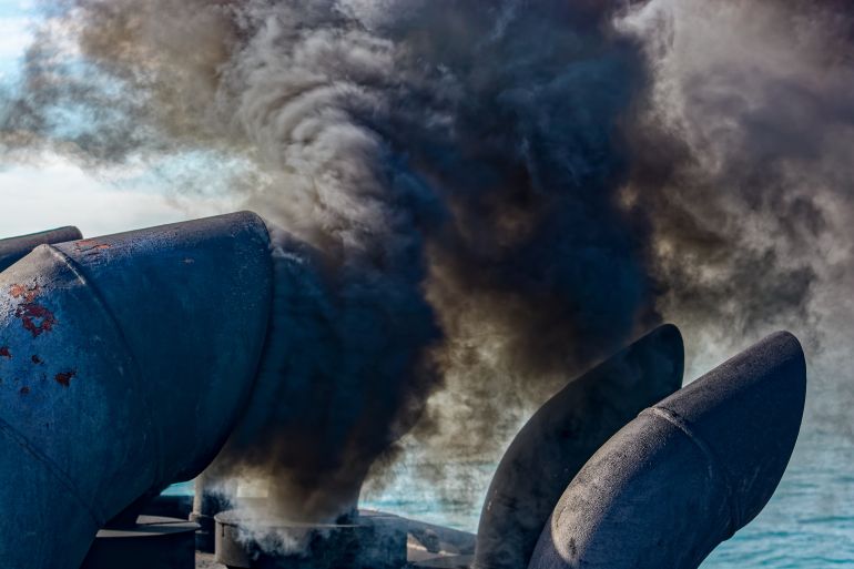 Close-up view of black exhaust fumes coming from the chimney of an moored vessel after main engine ignition.