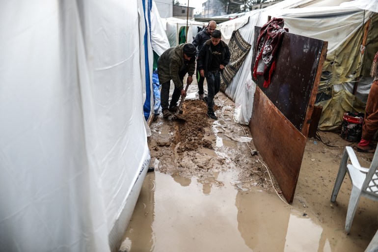 نازح من أهل غزة يتعامل مع المياه التي غمرت خميته في مدينة دير البلح (الأناضول)