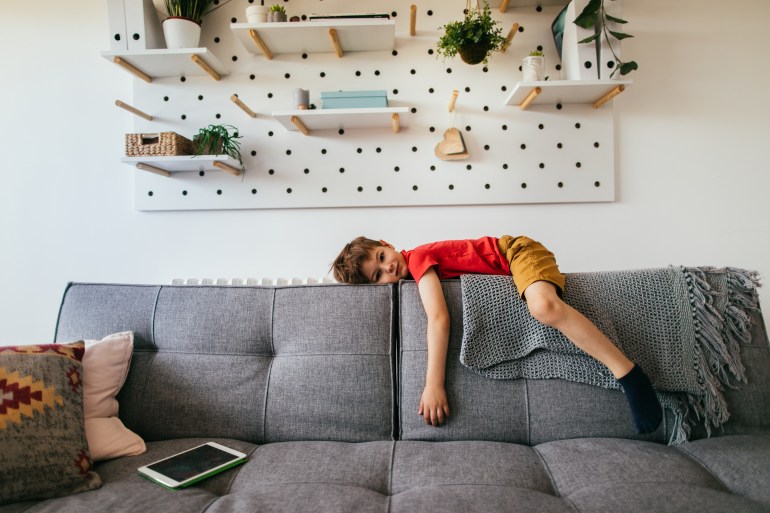 Photo of a little boy who is being bored, lying down on the sofa in his living room