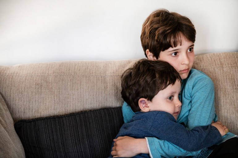 Big brother hugging toddler, staring in disbelief on sofa - stock photo