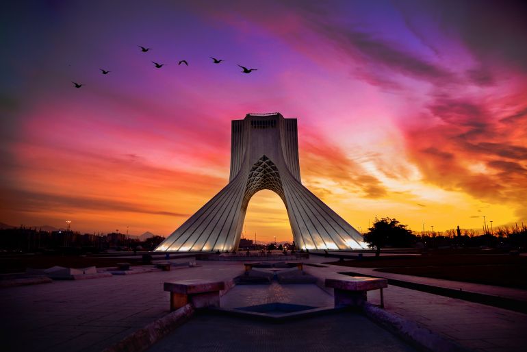 The sunset sky glows gold and orange over the Azadi Tower in Tehran, Iran