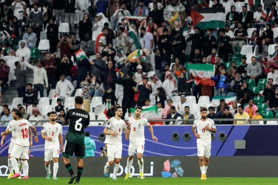 A spectator holds up the flag of Palestine in the stands as Iran's forward #09 Mehdi Taremi celebrates with his teammates after scoring their first goal during the Qatar 2023 AFC Asian Cup Group C football match between Iran and United Arab Emirates at Education City Stadium in al-Rayyan, west of Doha, on January 23, 2024. (Photo by KARIM JAAFAR / AFP)