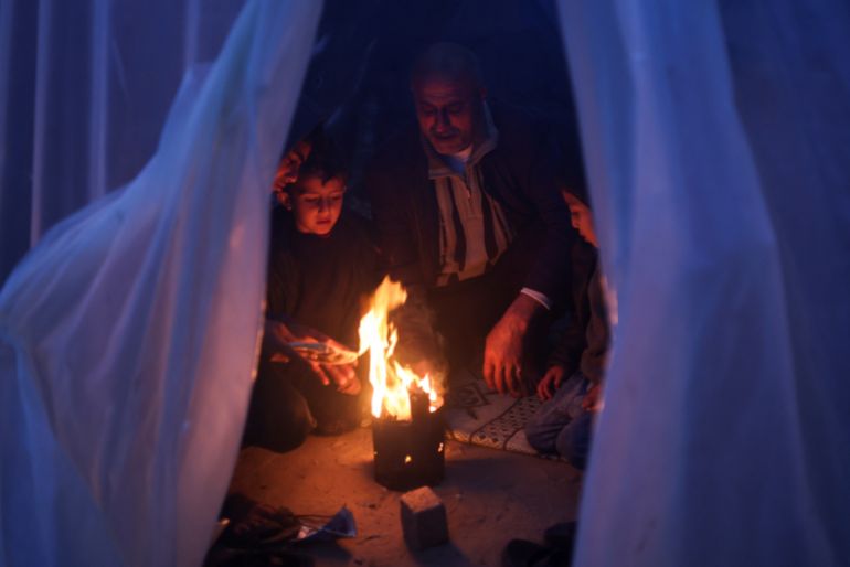 Displaced Palestinians, who fled their houses due to Israeli strikes, warm themselves by a fire on a rainy cold day at a tent camp, amid the ongoing conflict between Israel and Hamas, in Rafah in the southern Gaza Strip January 26, 2024. REUTERS/Saleh Salem