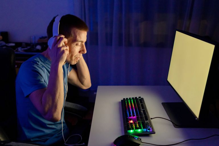 One mid adult man play computer video game in dark room, use neon colored rgb mechanical keyboard