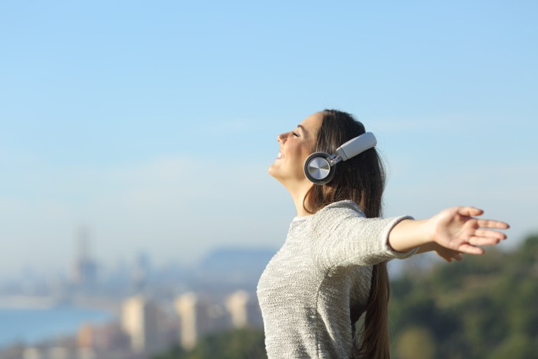 Girl listening to music with headphones breathing with wide open arms feeling free outdoors