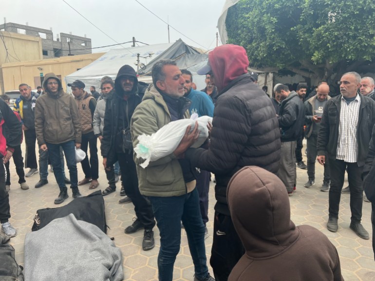 : تشرين ياغي يحمل جثمان حفيدته "أيلول" (عامان) ابنة الصحفي "محمد" قبيل مواراتها الثرى.