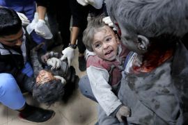 طفلة تنزف دما تحمل شقيقها المصاب بينما يحاول الأطباء في مستشفى شهداء الأقصى إسعاف الثالث الذي يعاني إصابات خطيرة نتيجة القصف الإسرائيلي على دير البلح (الأناضول)