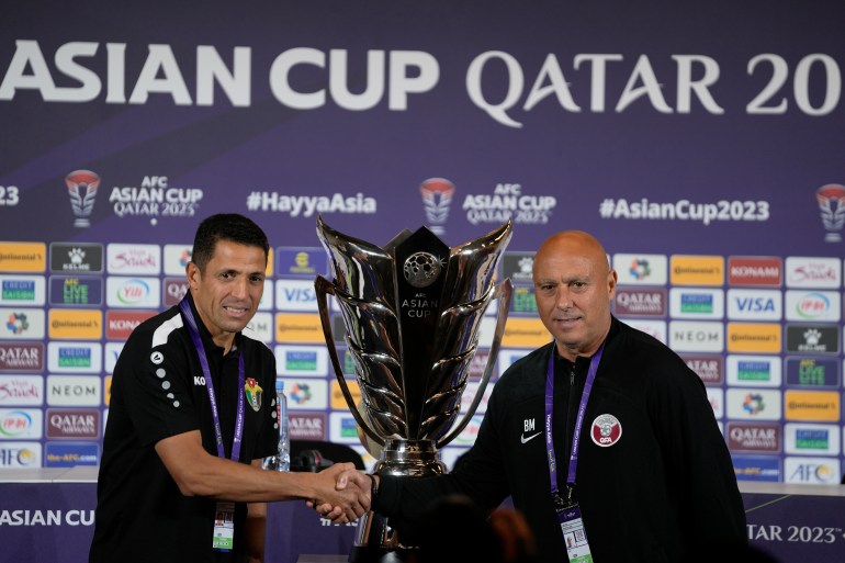 Jordan's head coach Lhoussanine Ammouta, left, and Qatar's head coach Bartolome Marquez shake hands in front of the Asian Cup trophy ahead of a press conference in Doha, Qatar, Friday, Feb. 9, 2024. Jordan will play Qatar on Saturday for the soccer final of the Asian Cup. (AP Photo/Thanassis Stavrakis)