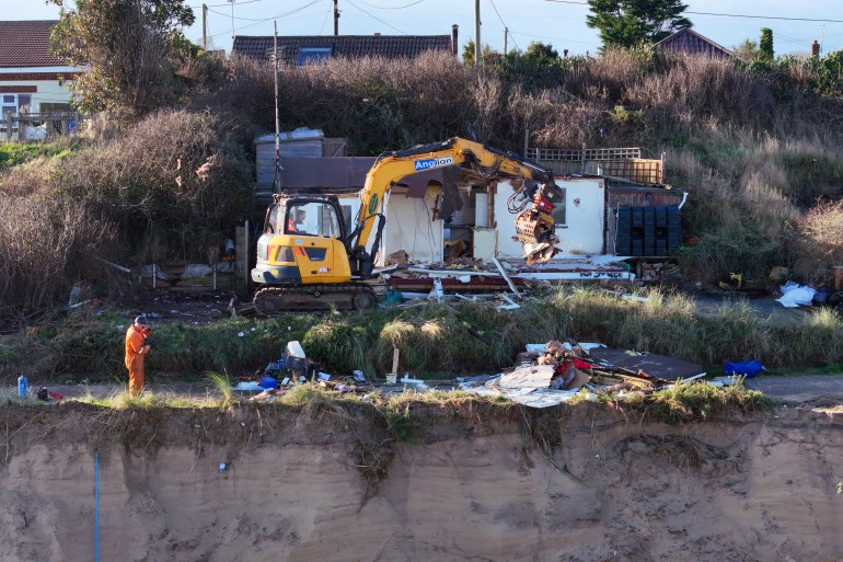 HEMSBY, ENGLAND - DECEMBER 11: In this aerial view a beach chalet is demolished by workers before it falls down the sea cliff on The Marrams at Hemsby Beach on December 11, 2023 in Hemsby, England. The collapse of a private access road in November, prompted by high tides and winds, led Great Yarmouth Borough Council to declare the rapidly eroding homes on The Marrams 'not structurally sound and unsafe.' This demolition coincides with the 10th anniversary of five village houses lost to the sea in 2013 when storms undermined foundations by stripping away significant sand. (Photo by Christopher Furlong/Getty Images)