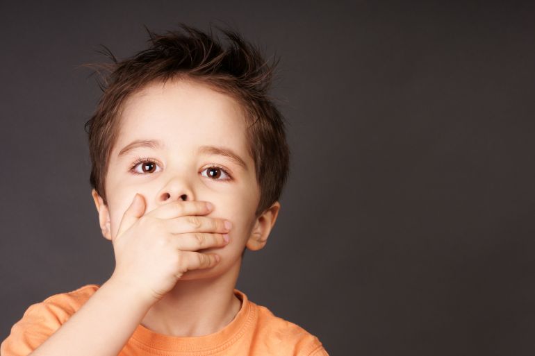 Portrait of cute little boy closed mouth with his hand, studio shot