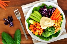 Healthy lunch bowl with avocado, hummus and fresh vegetables, overhead scene on wooden table