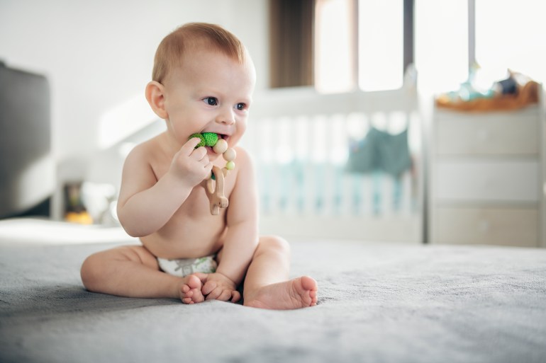 Portrait of adorable little baby boy at home playing with a wooden teething toy.