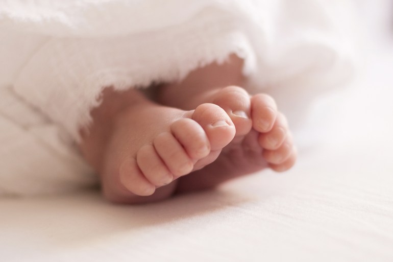 Feet of a newborn baby wrapped in white cloth close-up.