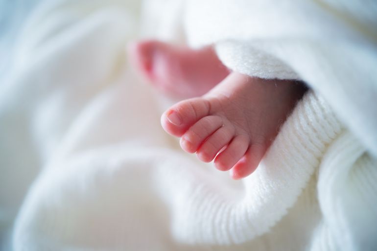 Close up of tiny adorable bare pink baby feet as the infant sleeps on white blanket