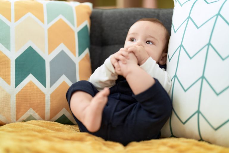 Adorable toddler sitting on sofa sucking feet at home