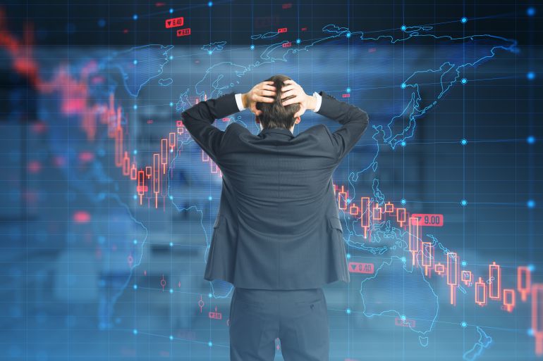 A businessman with head in hands standing before a futuristic screen displaying world maps and financial data indicating a global economic downturn