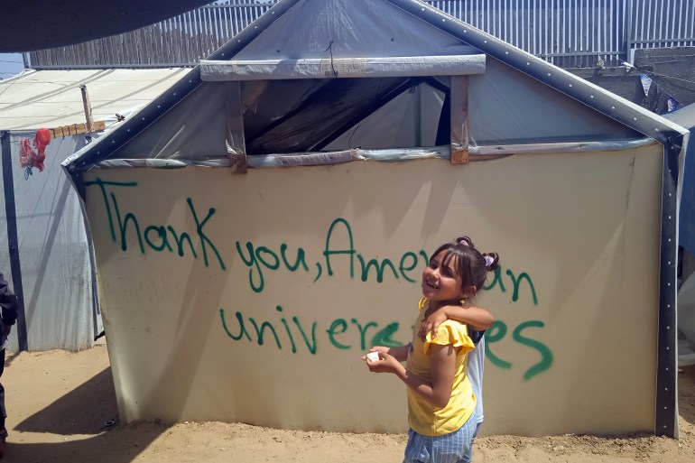 طفلة نازحة تبتسم أمام خيمة كتبت عليها عبارات شكر لطلبة الجامعات الأمريكية-رائد موسى-رفح-الجزيرة نت