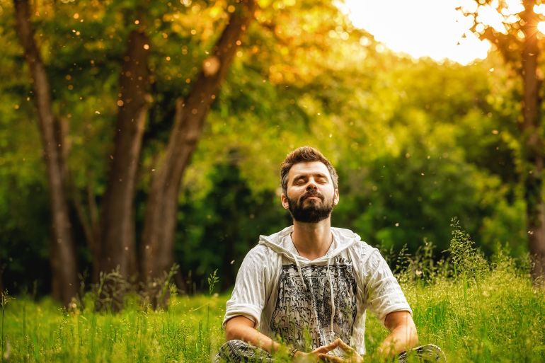 A man sitting on grass in the park and smiling with eyes closed by maxpetrov @ادوبي ستوك