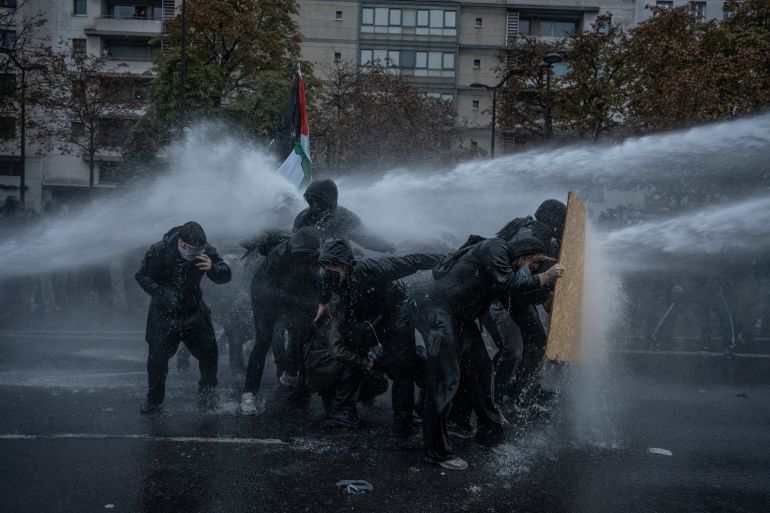 PARIS, FRANCE - OCTOBER 24: A group of protesters shield themselves from a water cannon during a protest on the streets of Paris on October 24, 2026 in Paris, France. Authorities in French cities and towns have imposed curfews, restrictions on movement, and some outright bans on demonstrations planned for October 24, following outbreaks of violence and looting on the fringes of the mostly peaceful protests that took place on October 17. French President Emmanuel Macron called for a ban on all demonstrations that were not organized by trade unions, and urged a return to calm. Nationwide demonstrations in France have gained momentum in recent weeks, sparked by student protests over poor conditions in the education system, and spiraling into overall discontent with the cost of living. (Photo by Manu Brabo/Getty Images)