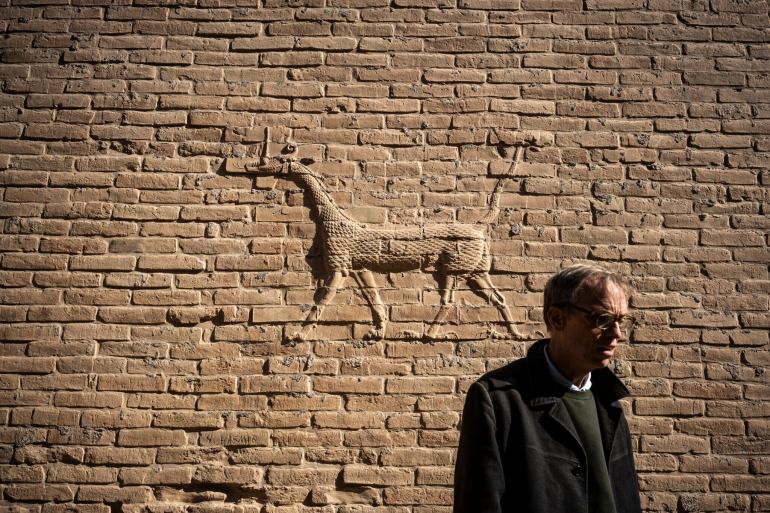 Jeff Allen has been working on the Babylon site since 2009. The 2,500-year-old dragon relief behind him is related to Marduk, the patron deity of Babylon.Credit...Abdullah Dhiaa Al-deen for The New York Times
